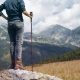 woman stands on rock and looks out across the landscape while holding a tactical walking stick
